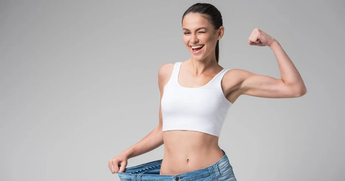 Confident woman flexing arm in too-large jeans after successful Weight Loss Treatment in DRAPER UT