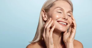 Middle-aged woman with blonde hair and glowing skin smiles during Sofwave™ in Draper, UT against a blue background.